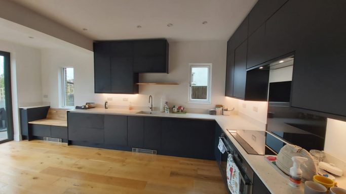Large kitchen with black door fronts light granite worktop, electric hob and wooden floor