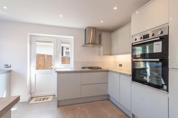 Gloss light grey kitchen, with stainless steel cooker hood, oven and tiled floor