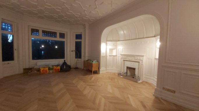 large lounge with molded ceiling and walls, large fire place and oak flooring