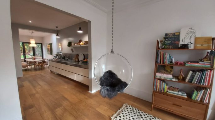 Open plan living area, wood floors, hanging chair, book cupboard with books