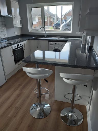 White fronted kitchen, with dark gloss worktop, wood effect vinyl plank flooring & two stools