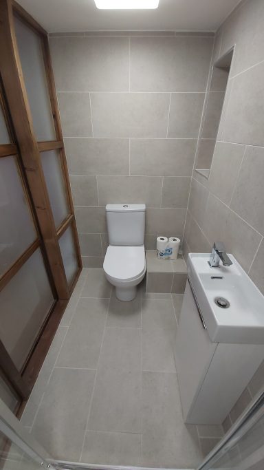 We built a timber framed wall forming an ensuite with enclosed shower, toilet & basin. Grey tiles on the walls