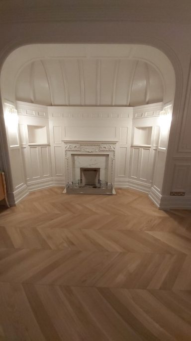 Large fire place decorated white with herringbone oak flooring