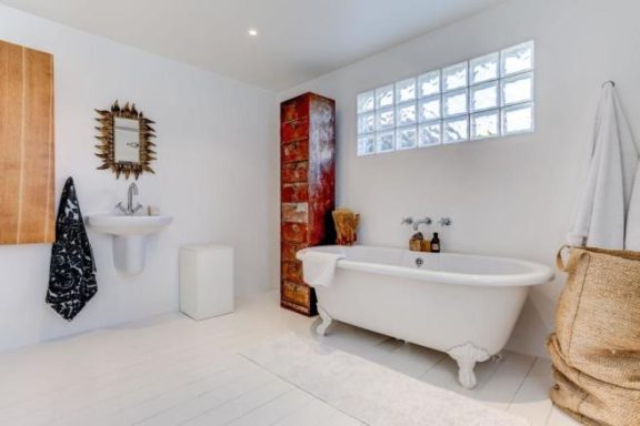 Bright white bathroom with free standing roll top bath, wall hung basin and glass blocks in the rear wall