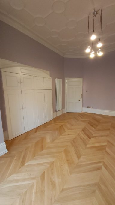 Large bedroom with fitted wardrobes, oak flooring. Molded ceiling with hanging light