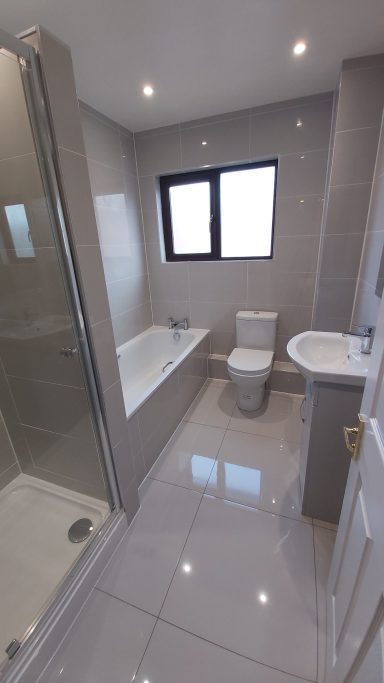 We installed a modern bathroom. With light grey polished tiles on walls & floor.  Enclosed shower, basin with vanity unit & bath